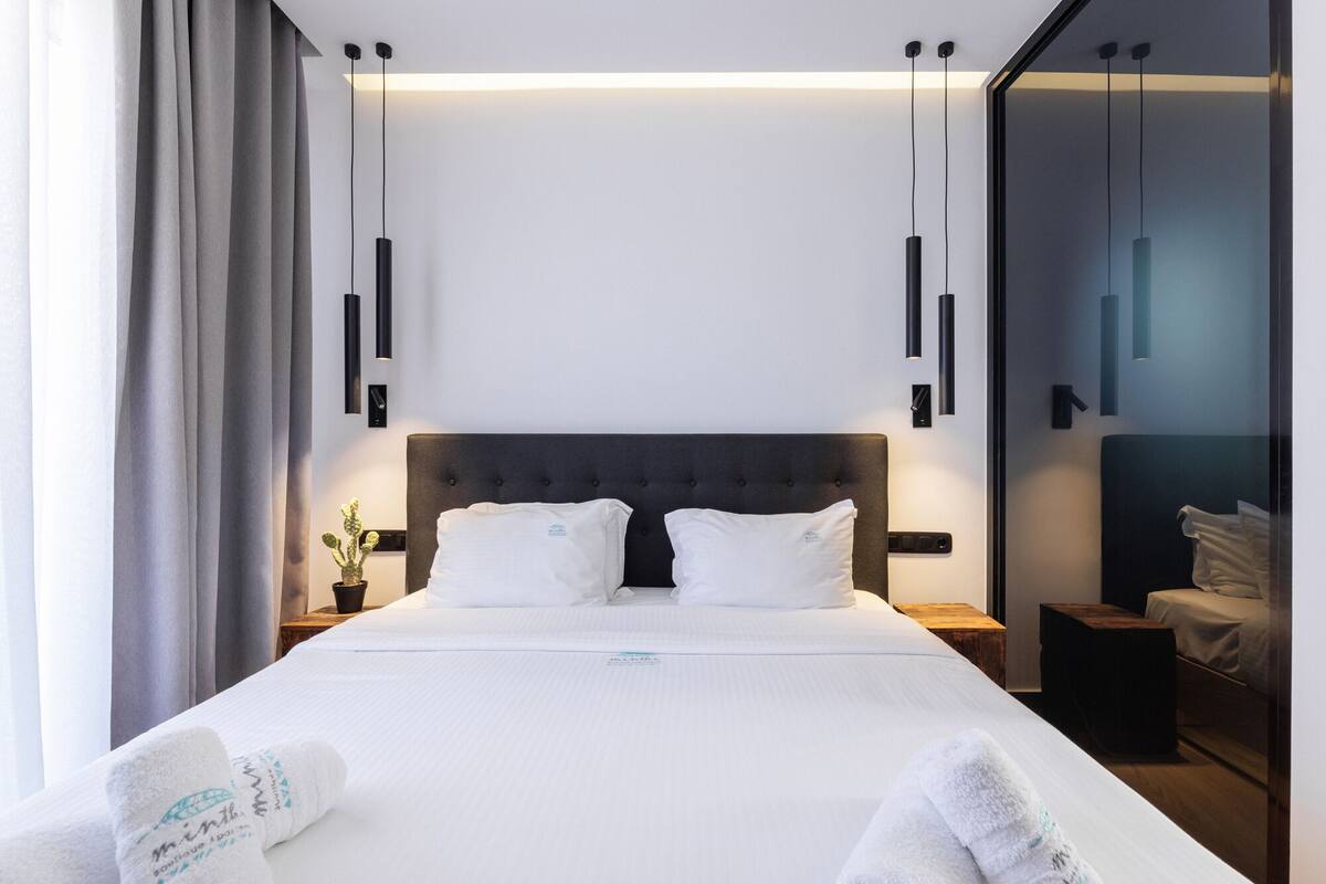 Ein modernes Hotelzimmer mit einem großen Bett, zwei Nachttischen, einer Stehlampe und einem Blick auf die Stadt, inklusive einer Zimmerpflanze.