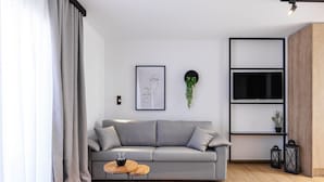 A modern living room with a grey sofa, a small wooden table, a mounted TV, and a wall-mounted shelf with plants. - Kentro Luxury Suites (Kassandra)