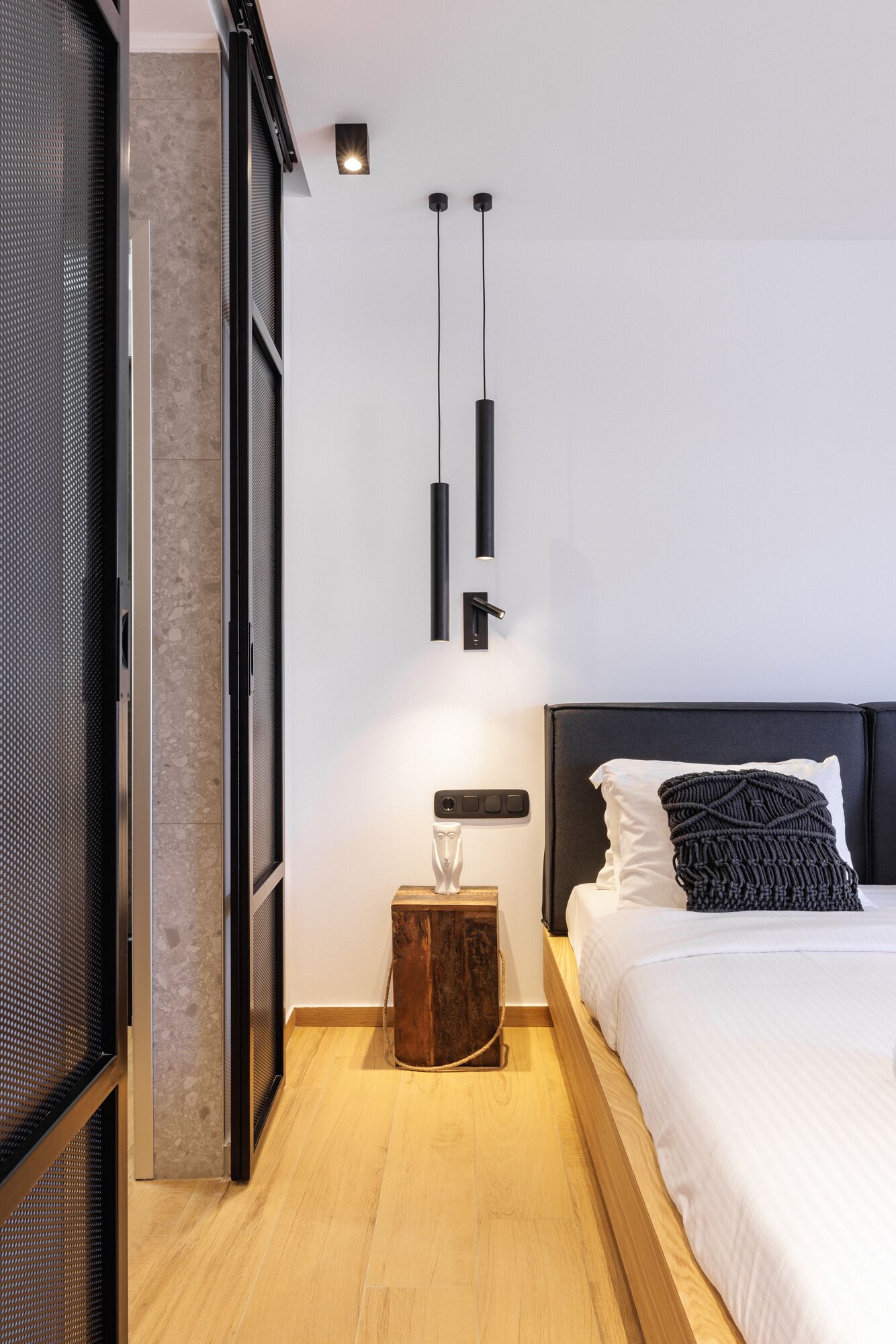 A modern bedroom with a bed, a nightstand, a wall-mounted light, and a textured wall.