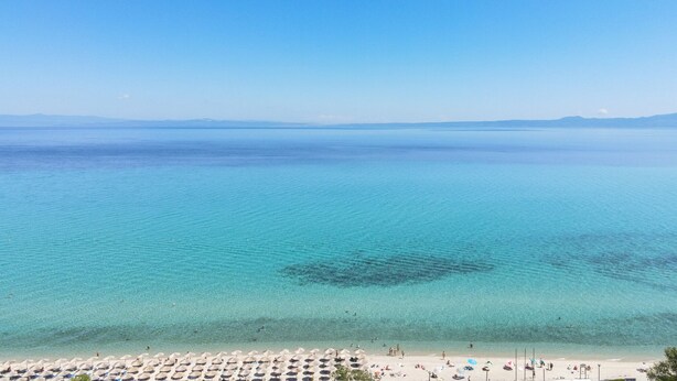 A beach with clear turquoise water, a sandy shore, and umbrellas. - Kentro Luxury Suites (Kassandra)