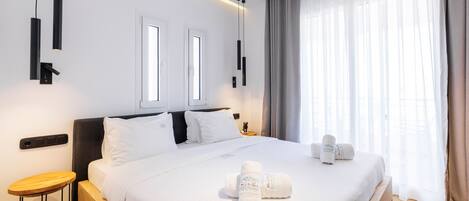 A hotel room with a large bed, two bedside tables, a small wooden stool, and a window with curtains.