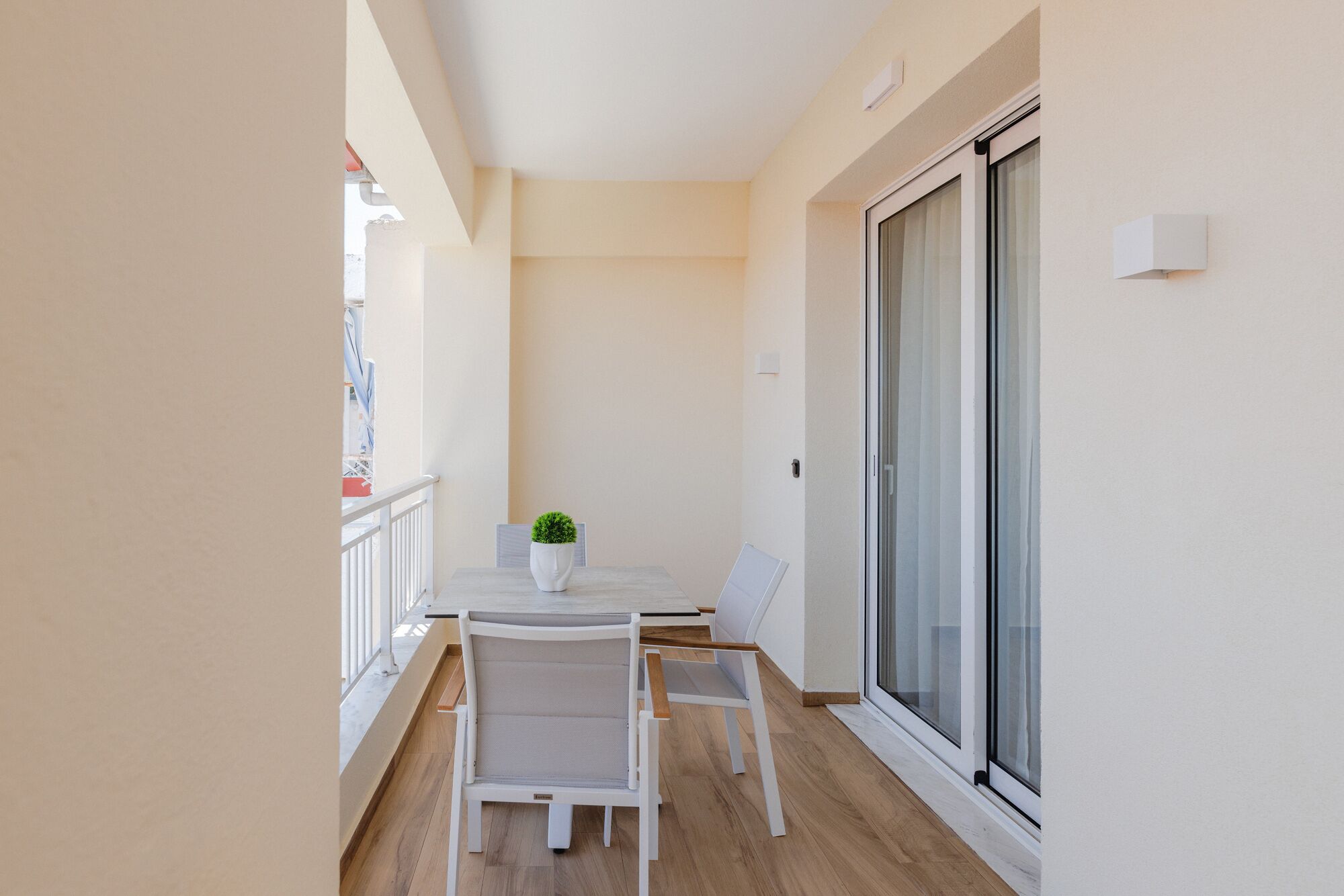 A balcony with a table and chairs, a potted plant, and a sliding glass door.