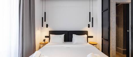 A modern hotel room with a large bed, two bedside tables, and a view of the city.