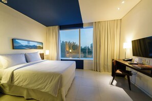 Een hotelkamer met een groot bed, een bureau met stoel, een televisie en een raam met gordijnen.