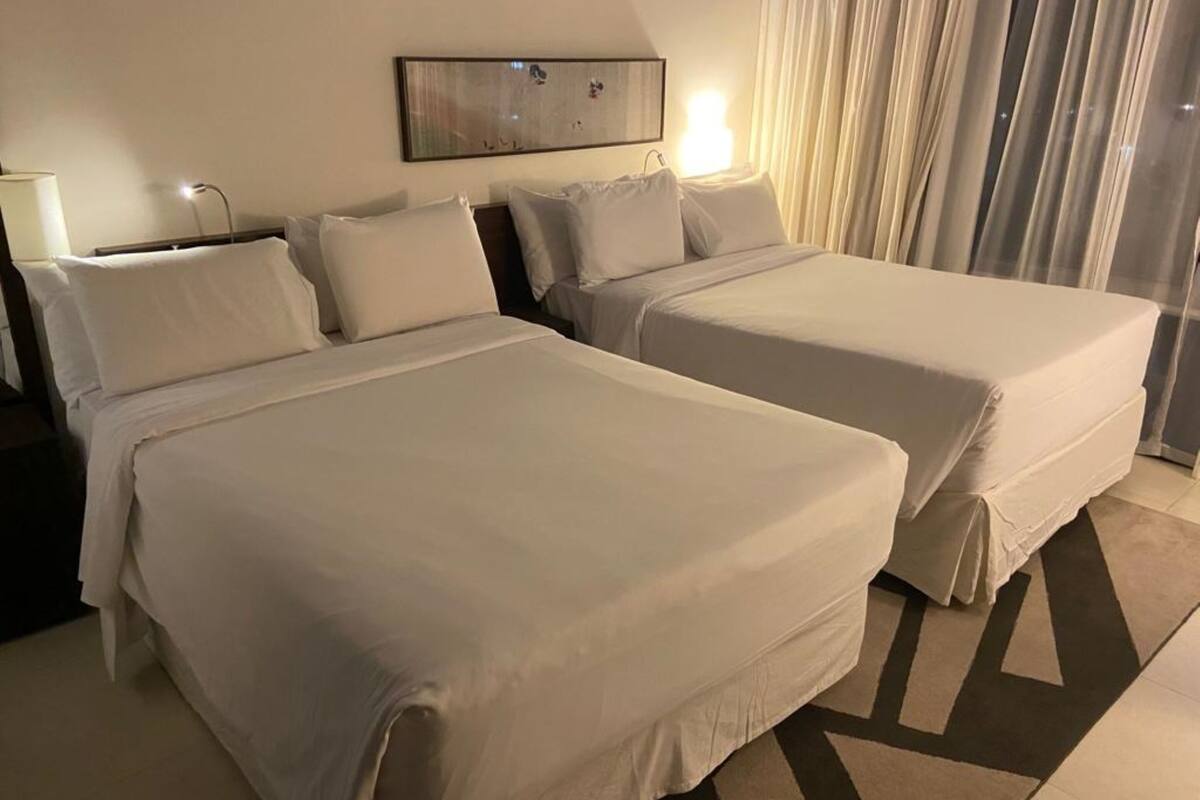 Een hotelkamer met twee bedden, een nachtkastje, een lamp en een lijst met een afbeelding aan de muur.