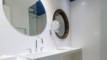 A modern bathroom with a white sink, a round mirror, and a wooden bench with towels.