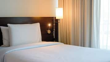 Uma cama bem arrumada com lençóis brancos, cabeceira de madeira e luminária fixada na parede.