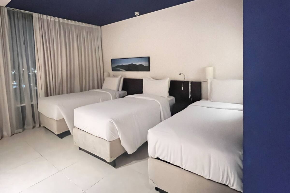 Een moderne hotelkamer met twee bedden, een groot raam met gordijnen, een flatscreen televisie en een schilderij aan de muur.