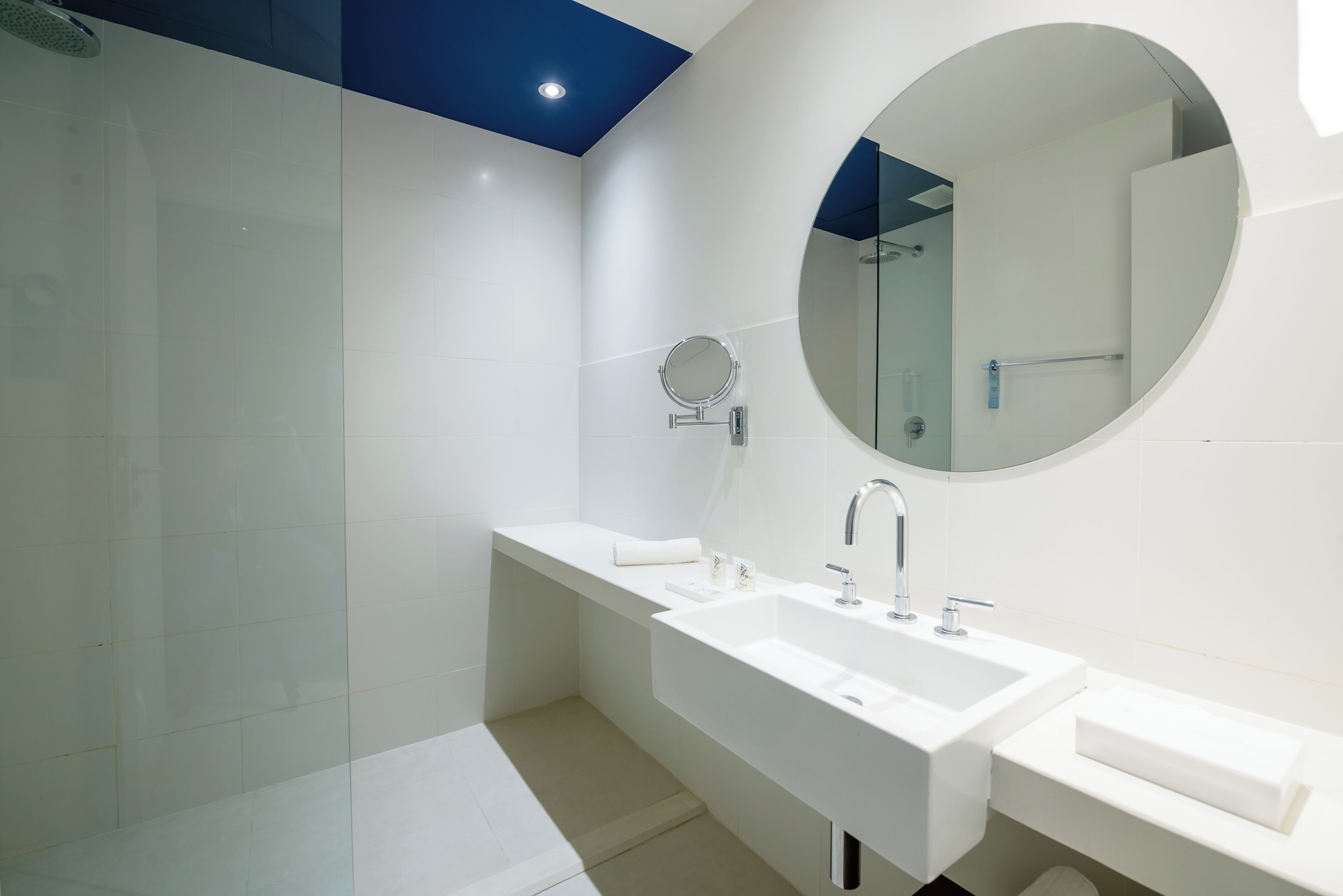Un baño moderno con un lavamanos grande, un espejo redondo y una zona de ducha.