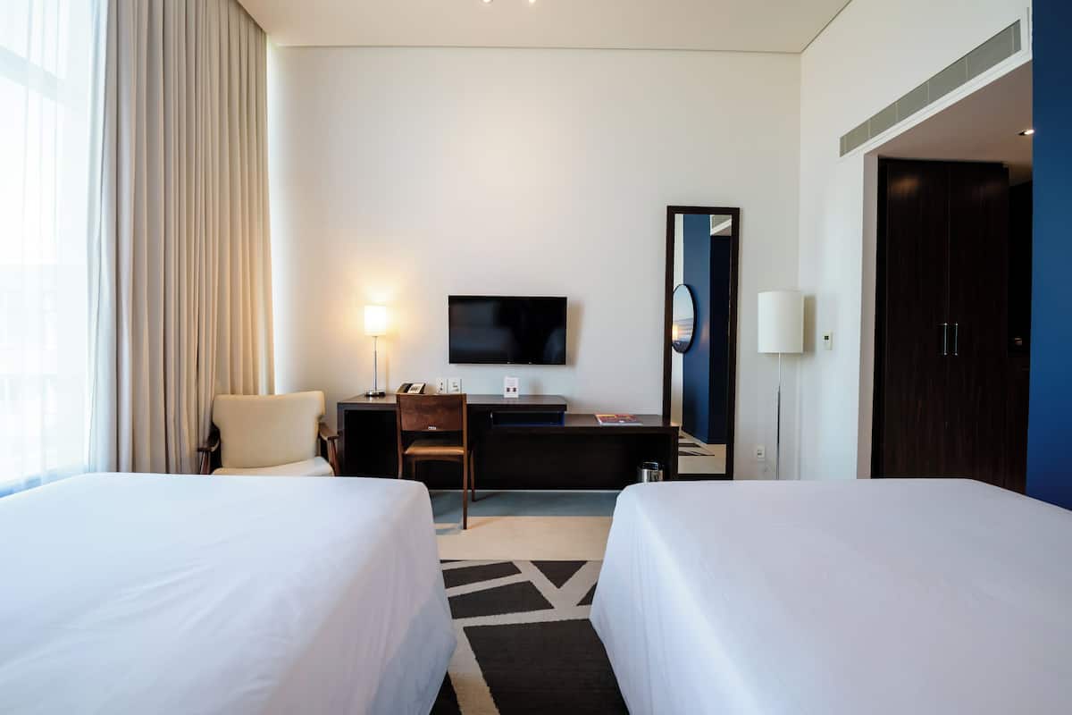 Een hotelkamer met twee bedden, een bureau met een televisie, een stoel, een lamp en een kledingkast.