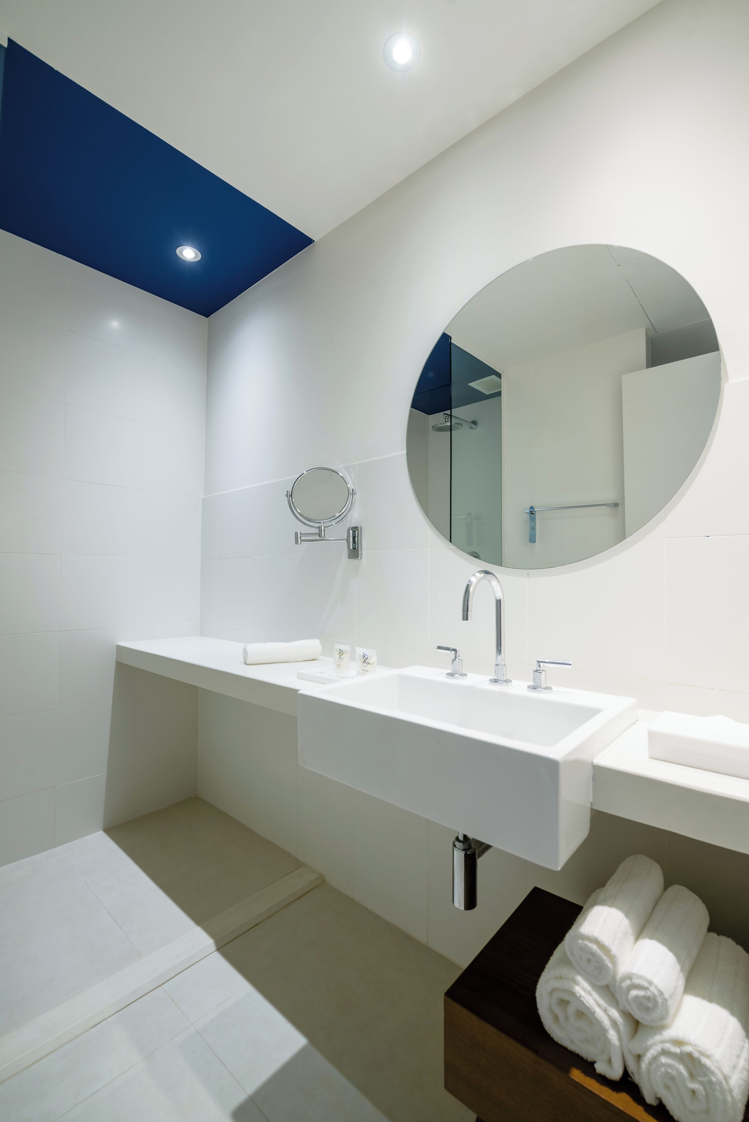 A modern bathroom with a white sink, a round mirror, and a blue accent wall.