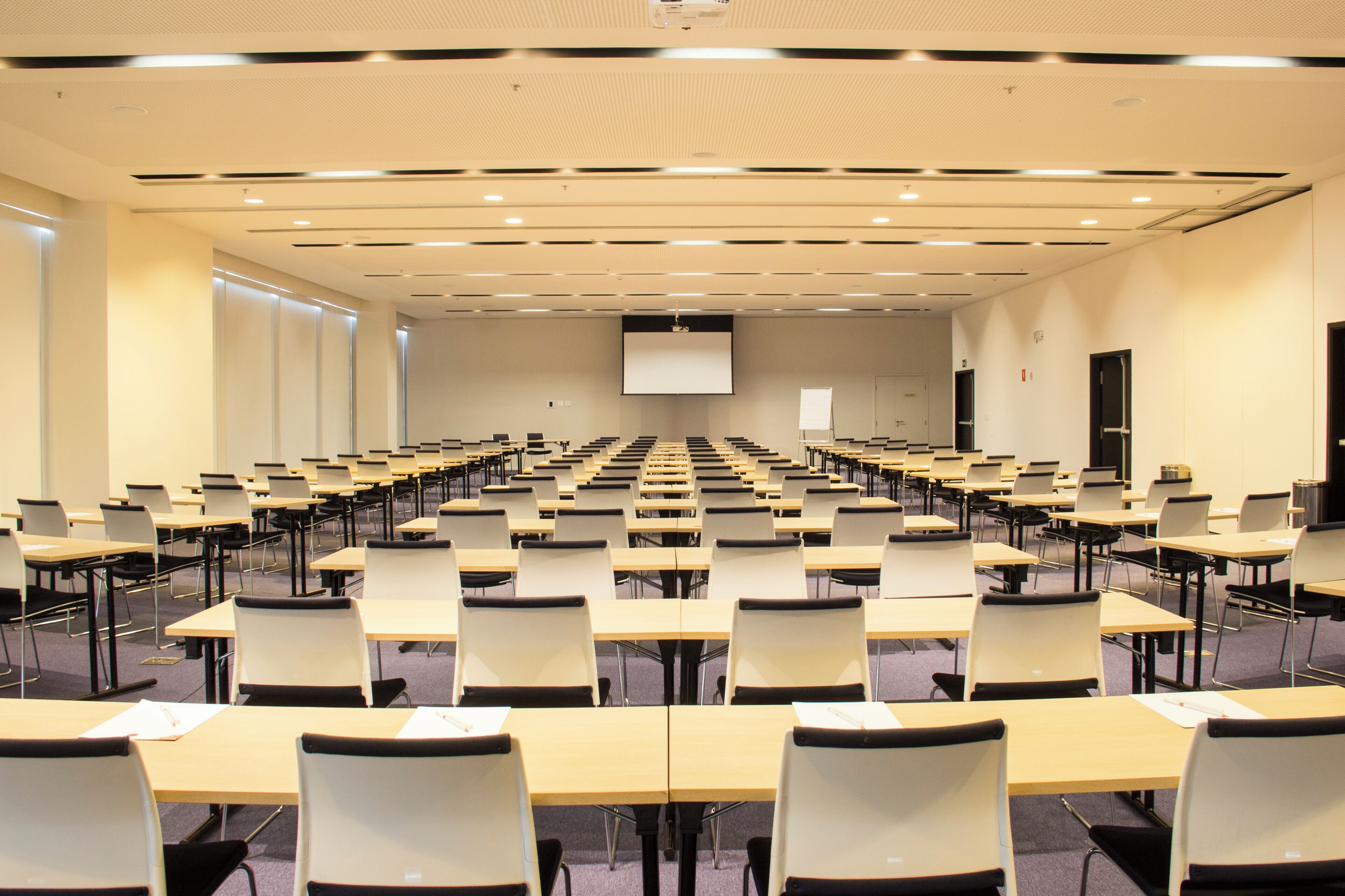 A conference room with rows of tables and chairs, a projector screen, and a whiteboard.