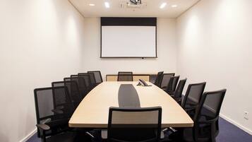 A conference room with a long table, black mesh chairs, a projector screen, and a whiteboard.