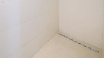 Casa de banho com paredes e chão em azulejo branco, um chuveiro e cabine de duche em vidro.