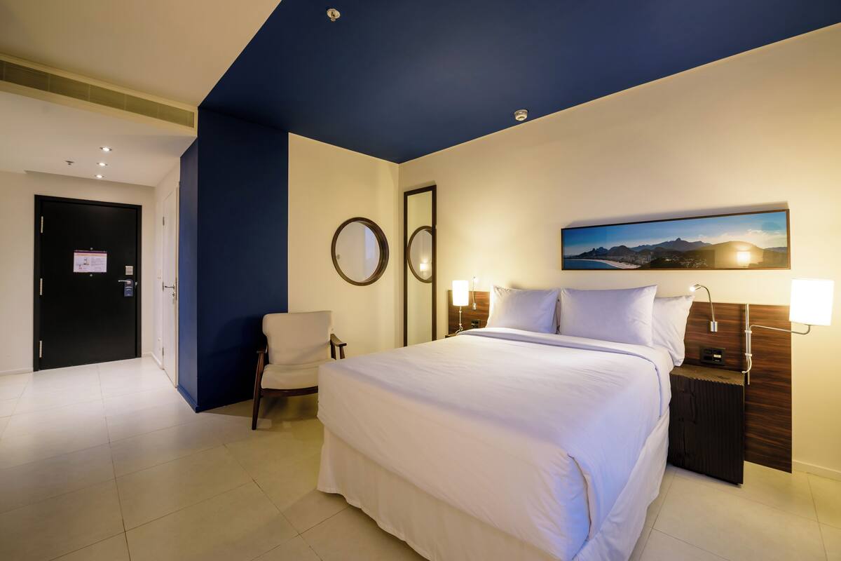 Een hotelkamer met een groot bed, een stoel, een bureau met lamp en een schilderij aan de muur.