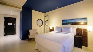 Una habitación de hotel con una cama grande, una silla, un escritorio con lámpara y un cuadro en la pared.