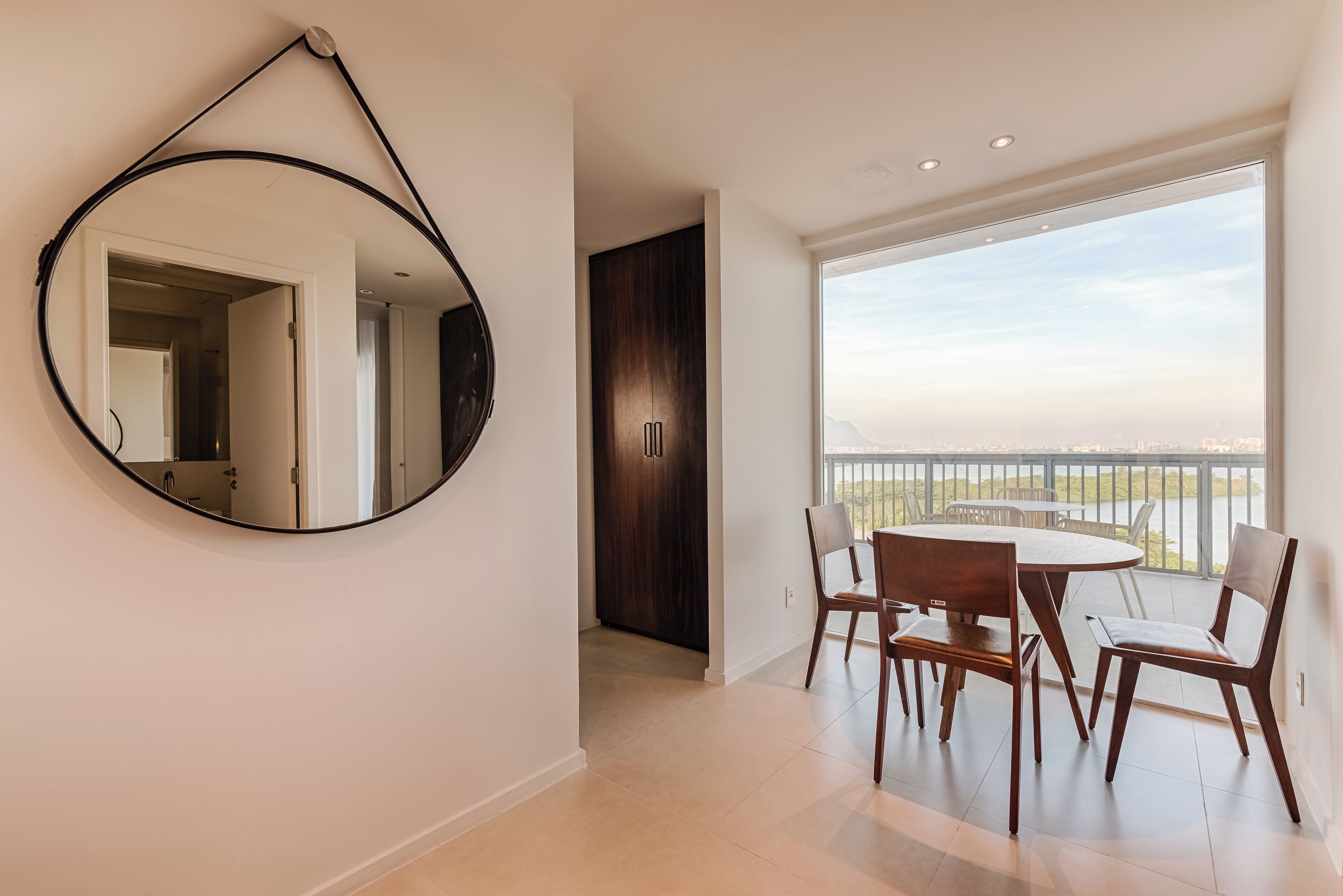 Un espace repas moderne avec une table ronde et des chaises, un grand miroir au mur et une vue sur un balcon doté d’une balustrade.