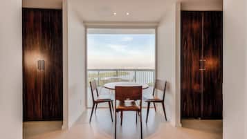 A modern dining area with a round table and four chairs, flanked by dark wooden cabinets, leading to a balcony with a view of the cityscape.