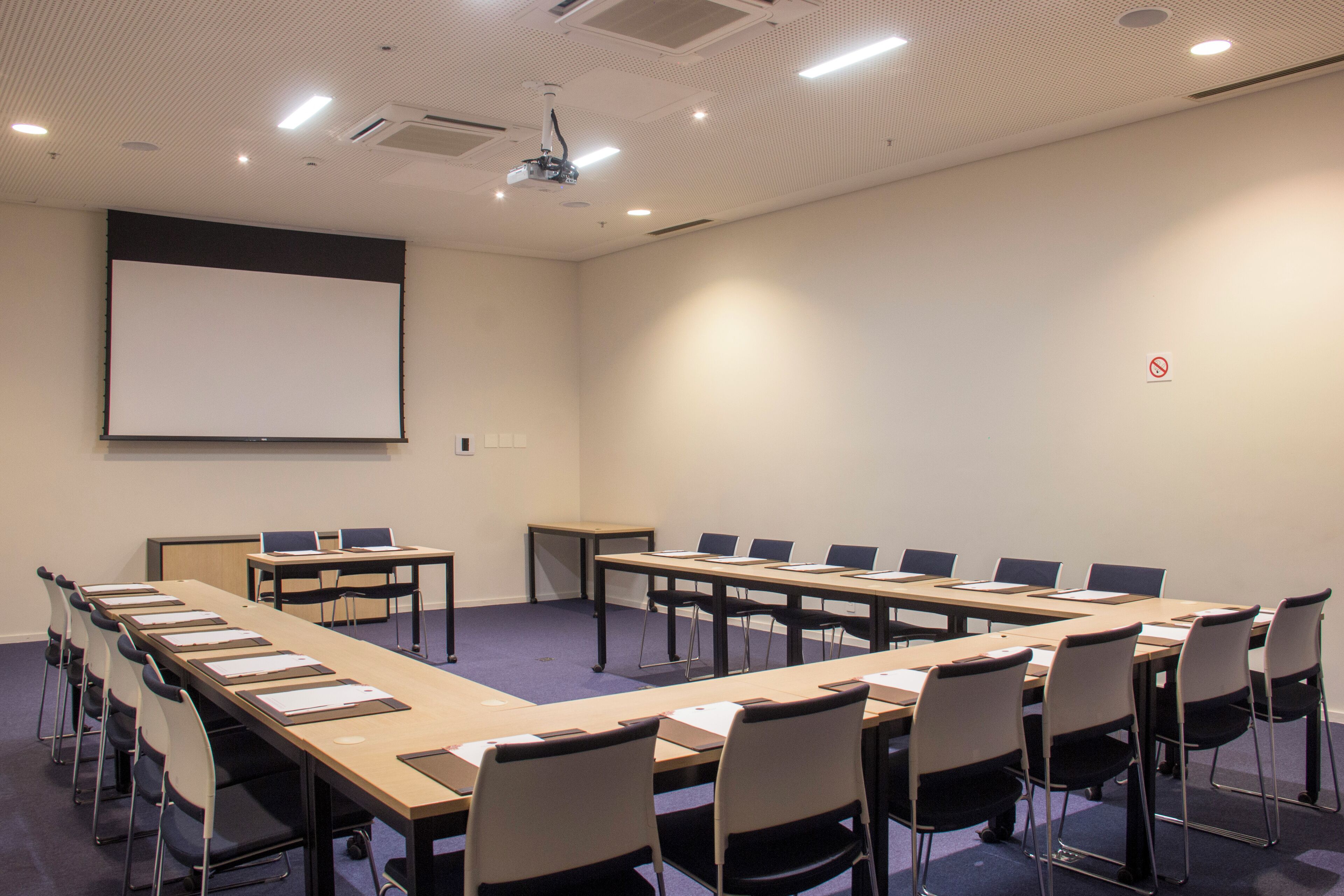 Un salón de conferencias con una larga mesa, sillas, una pantalla de proyector y una pizarra.