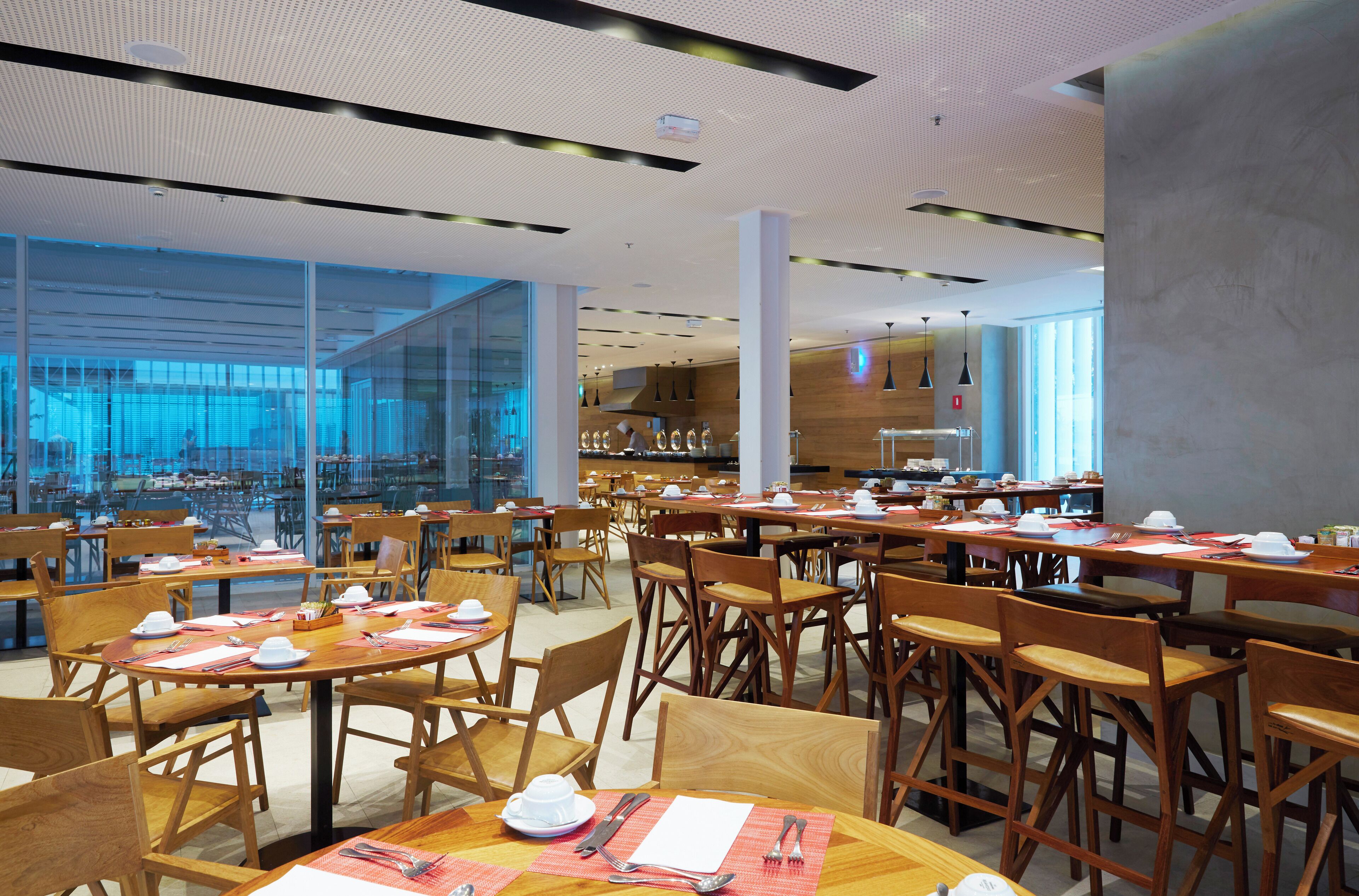Un comedor amplio con varias mesas y sillas, ventanas grandes y un diseño moderno de techo.