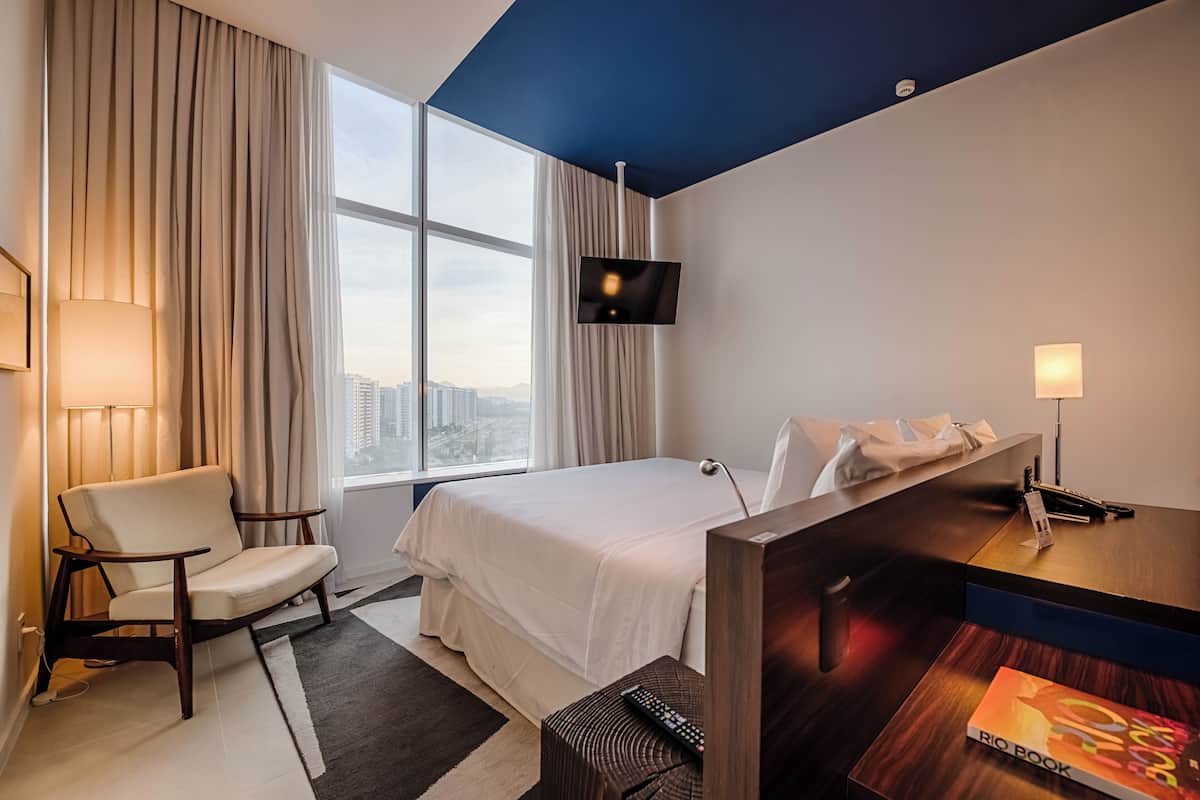 Een hotelkamer met een bed, een stoel, een bureau, een televisie en een raam met uitzicht op de stad.