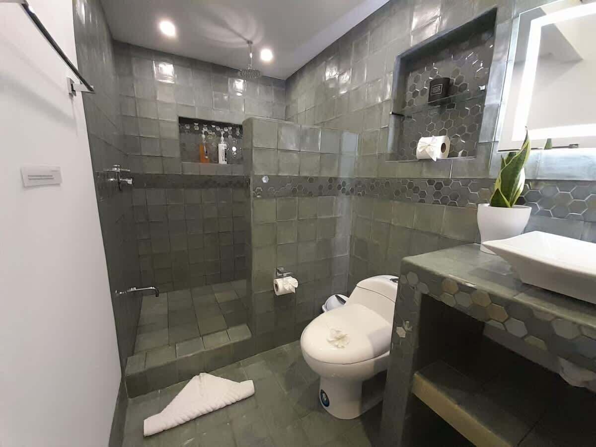A modern bathroom with a glass-enclosed shower, a toilet, and a sink with a decorative tile backsplash.