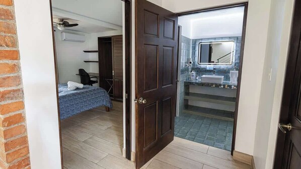 Une chambre comprenant un lit, un bureau, une chaise et une salle de bain avec un lavabo et un miroir.