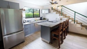 Une cuisine moderne dotée d’un îlot central, d’appareils électroménagers en acier inoxydable et d’un escalier avec une rampe en verre.