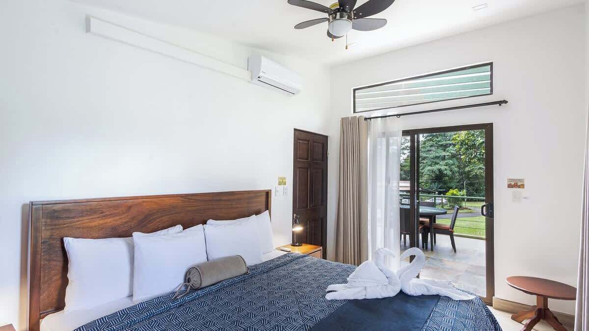 A hotel room with a large bed, a ceiling fan, an air conditioning unit, a sliding glass door to a patio, and a small table.