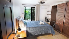 A bedroom with a bed, a desk with a lamp, a chair, a wardrobe, and a balcony with a view.