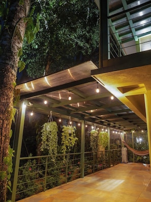 Un espacio al aire libre techado con plantas colgantes, una hamaca y una barandilla de metal.