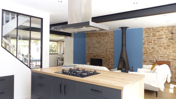A modern kitchen with a central island, a stone wall, and a fireplace.