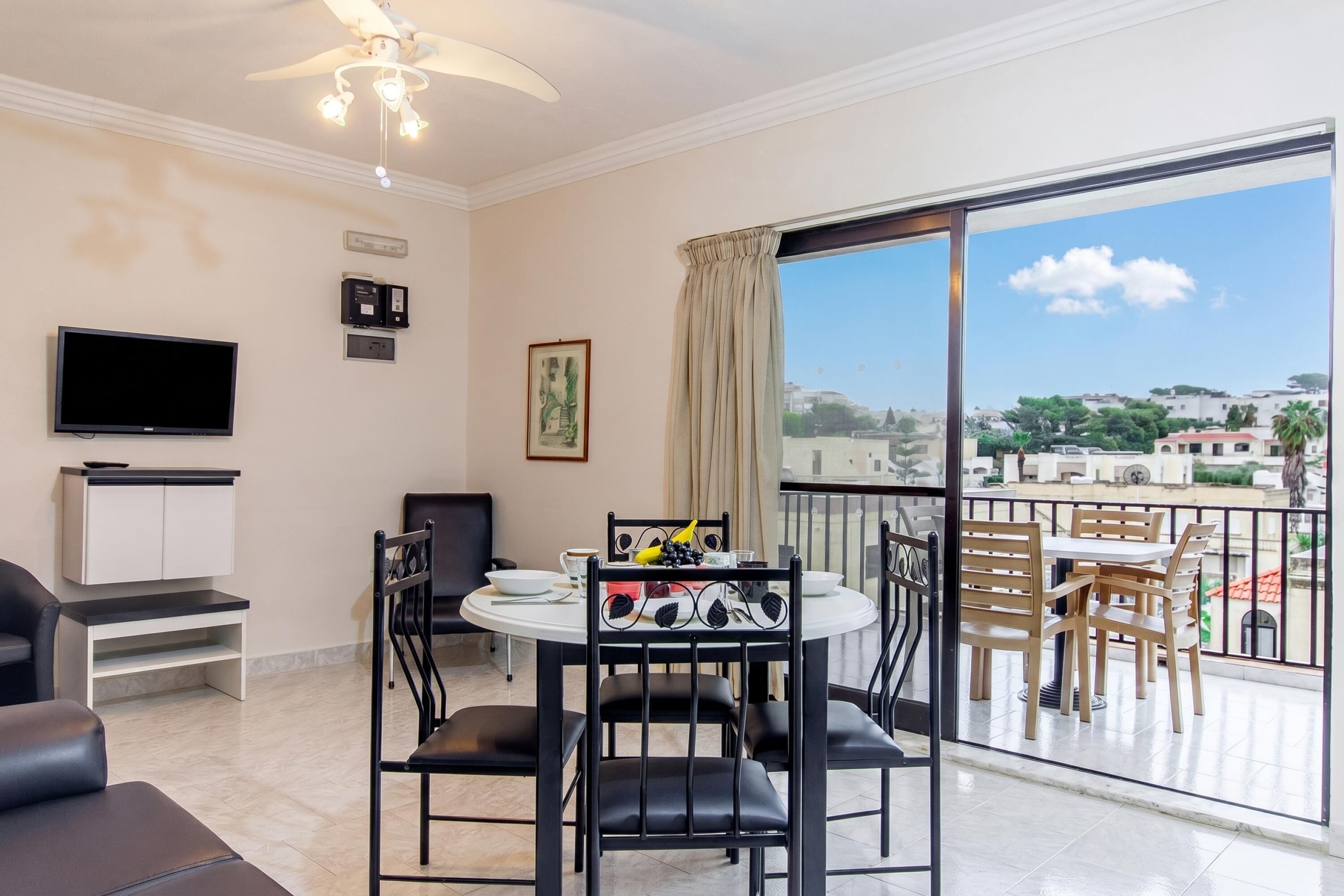 Una habitación con una mesa de comedor, sillas, televisión y un balcón con vistas.