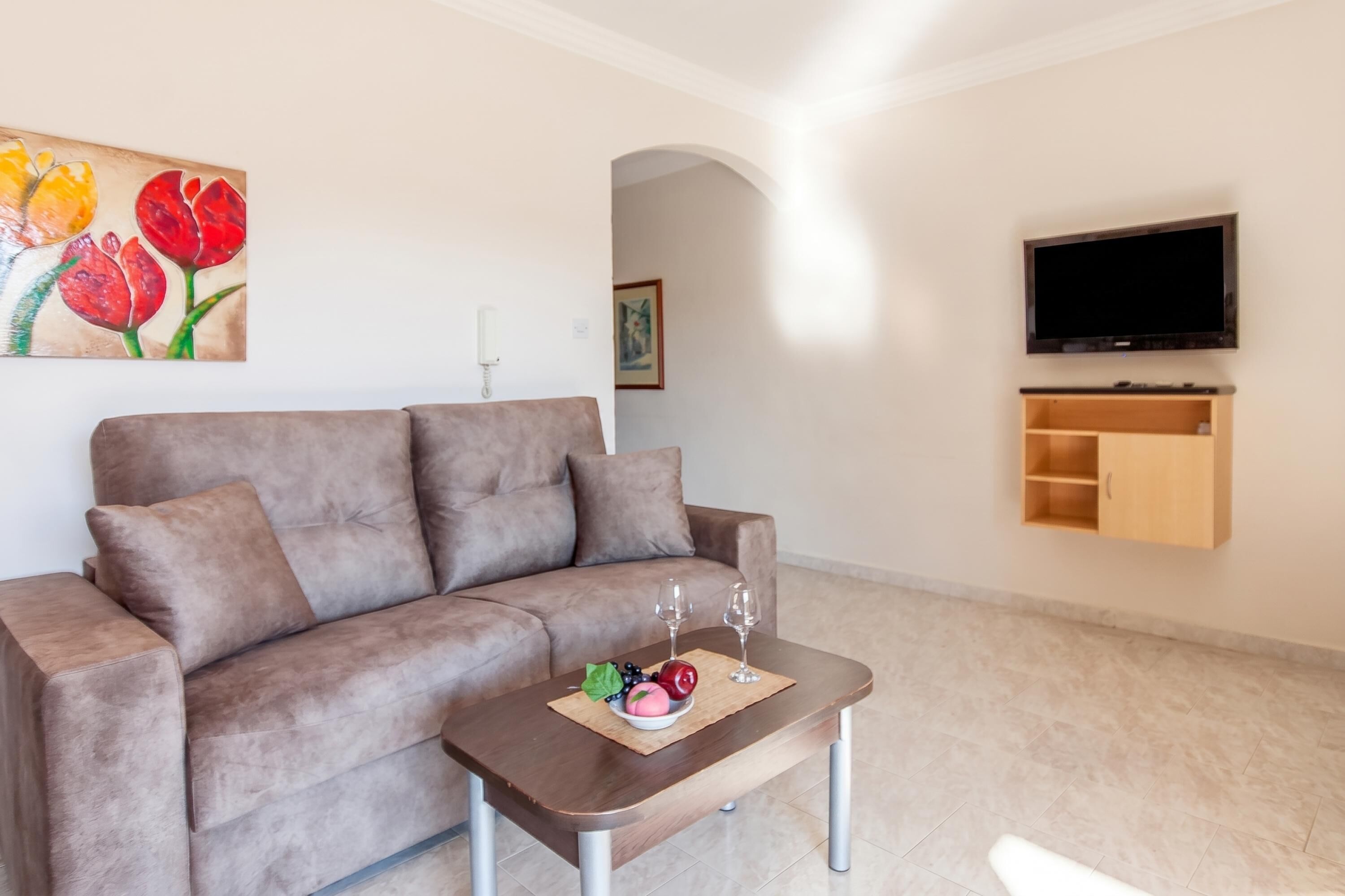A living room with a sofa, a coffee table with fruit and glasses, a TV, and a wooden cabinet.