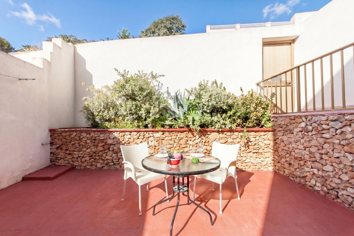 Un patio con una mesa redonda y cuatro sillas, un muro de piedra y una escalera.