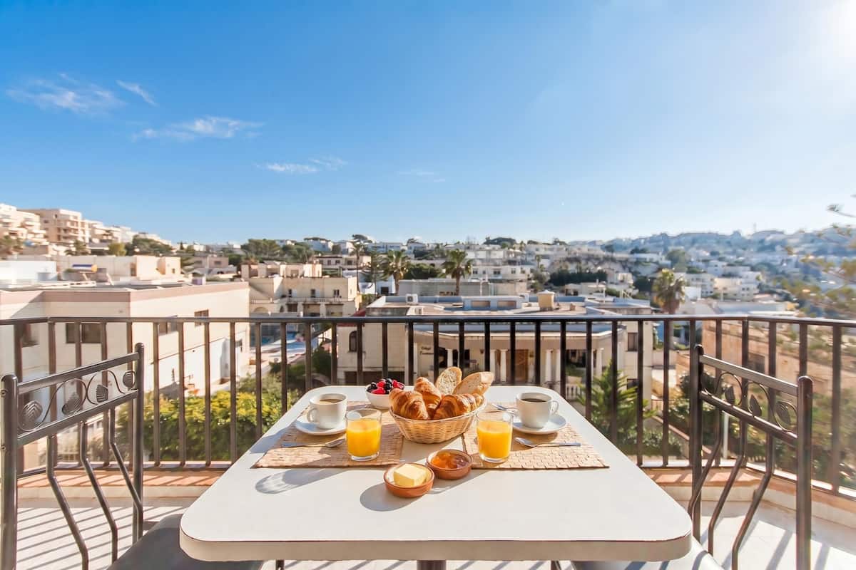 Un balcón con una mesa dispuesta para el desayuno, que incluye cruasanes, café y jugo de naranja.