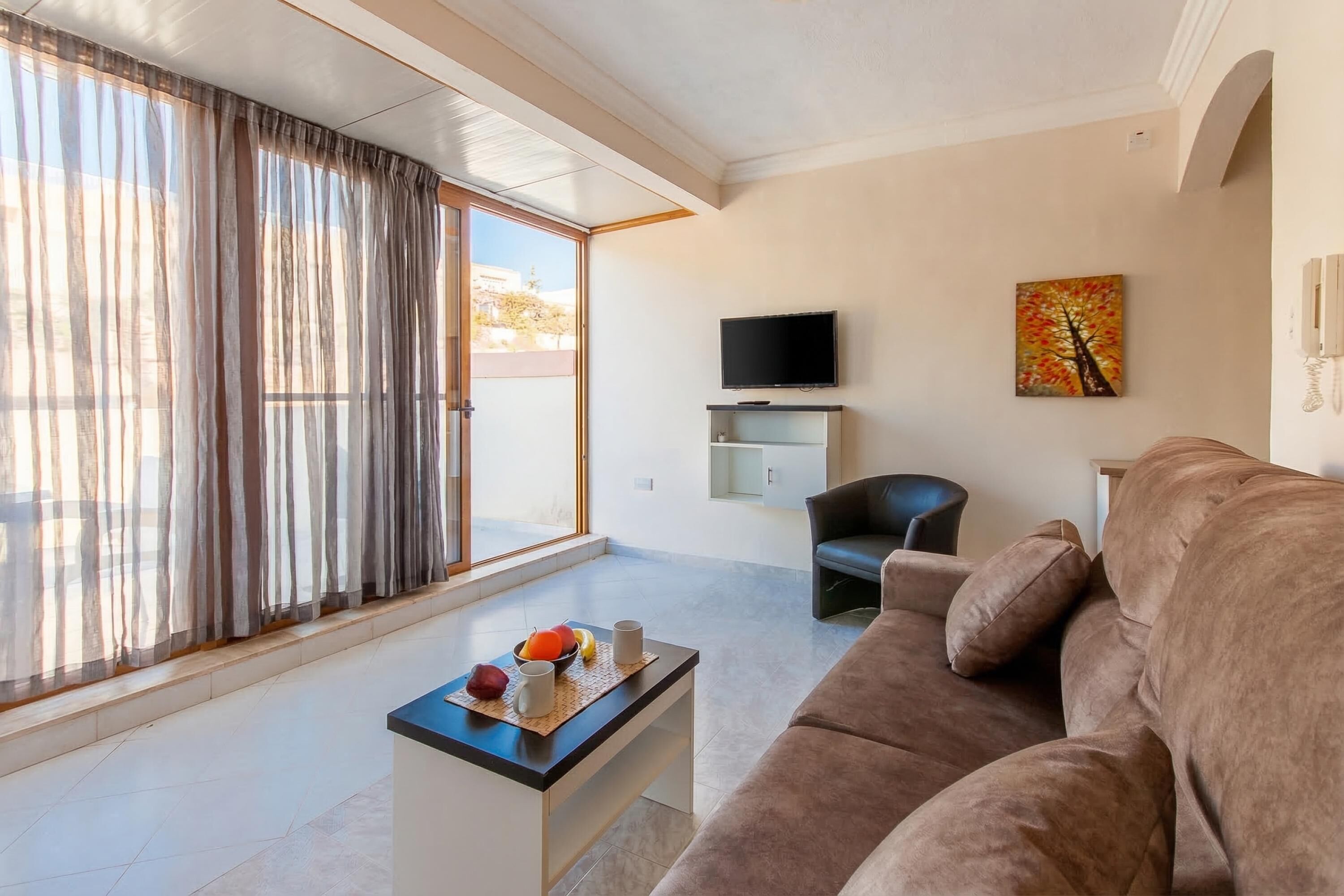 A modern living room with a sofa, a coffee table with fruit, a TV, and a painting on the wall.