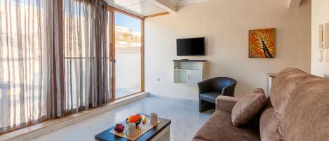 A modern living room with a sofa, a coffee table with fruit, a TV, and a painting on the wall.
