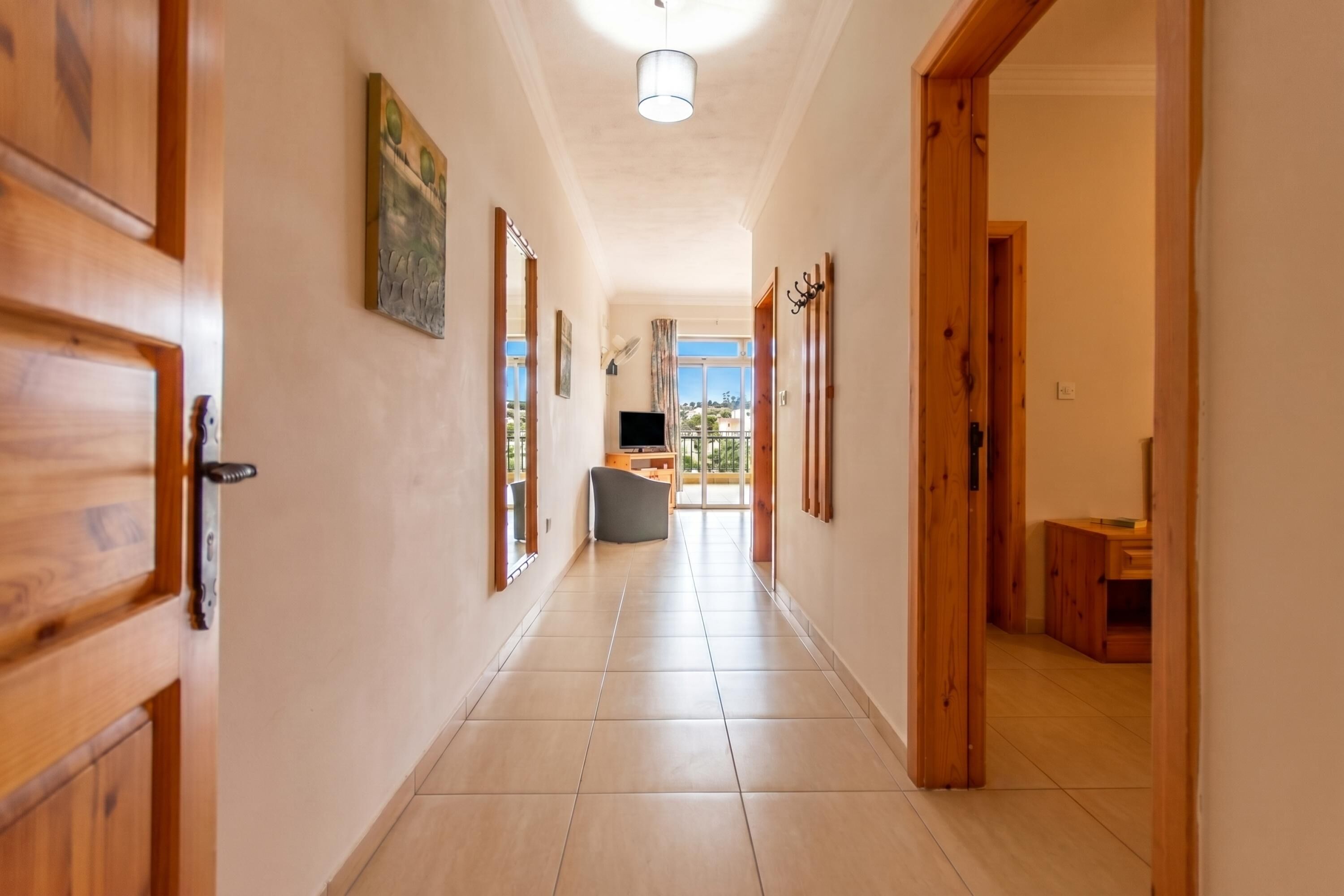 A hallway with wooden doors, a flat-screen TV, and a view of the outdoors.