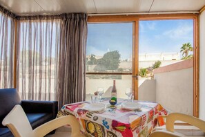 Un balcón con una mesa para dos, una silla y vistas a edificios y palmeras.