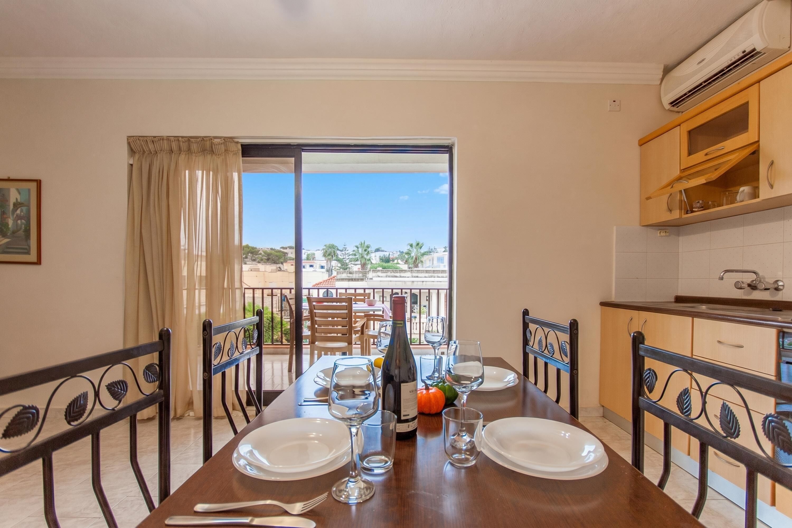 A dining area with a table set for four, a bottle of wine, and a view of the outdoors.