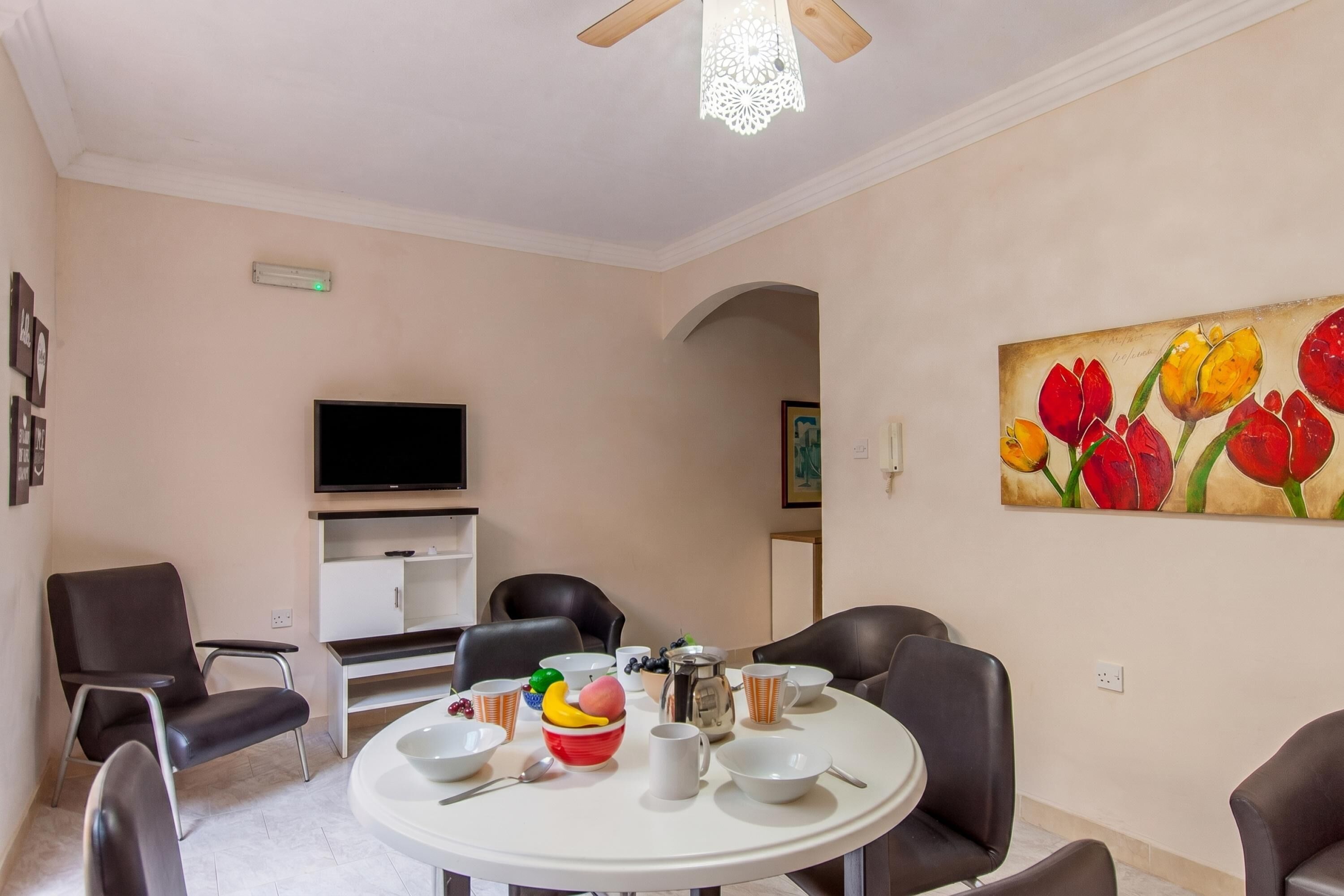 A dining area with a round table, chairs, and a painting of tulips on the wall.