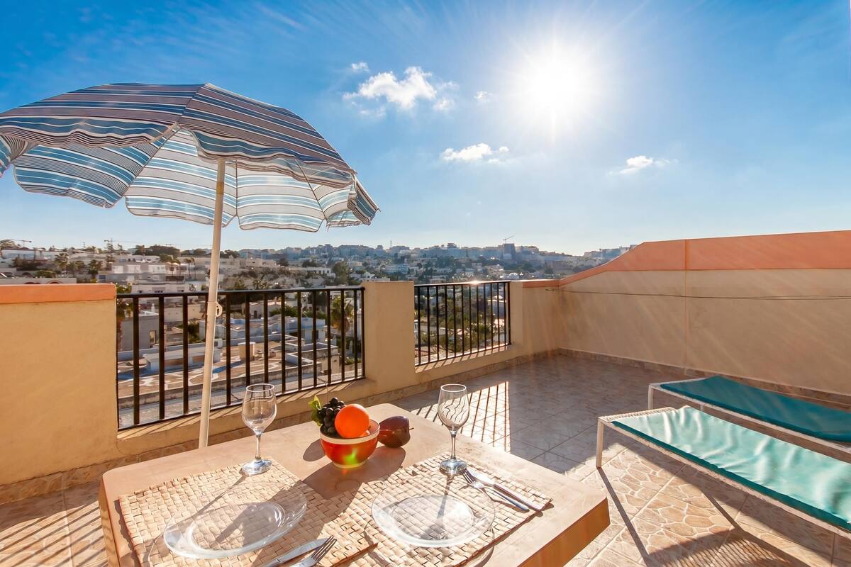 Una terraza con una mesa para dos, un paraguas a rayas y vistas a la ciudad.
