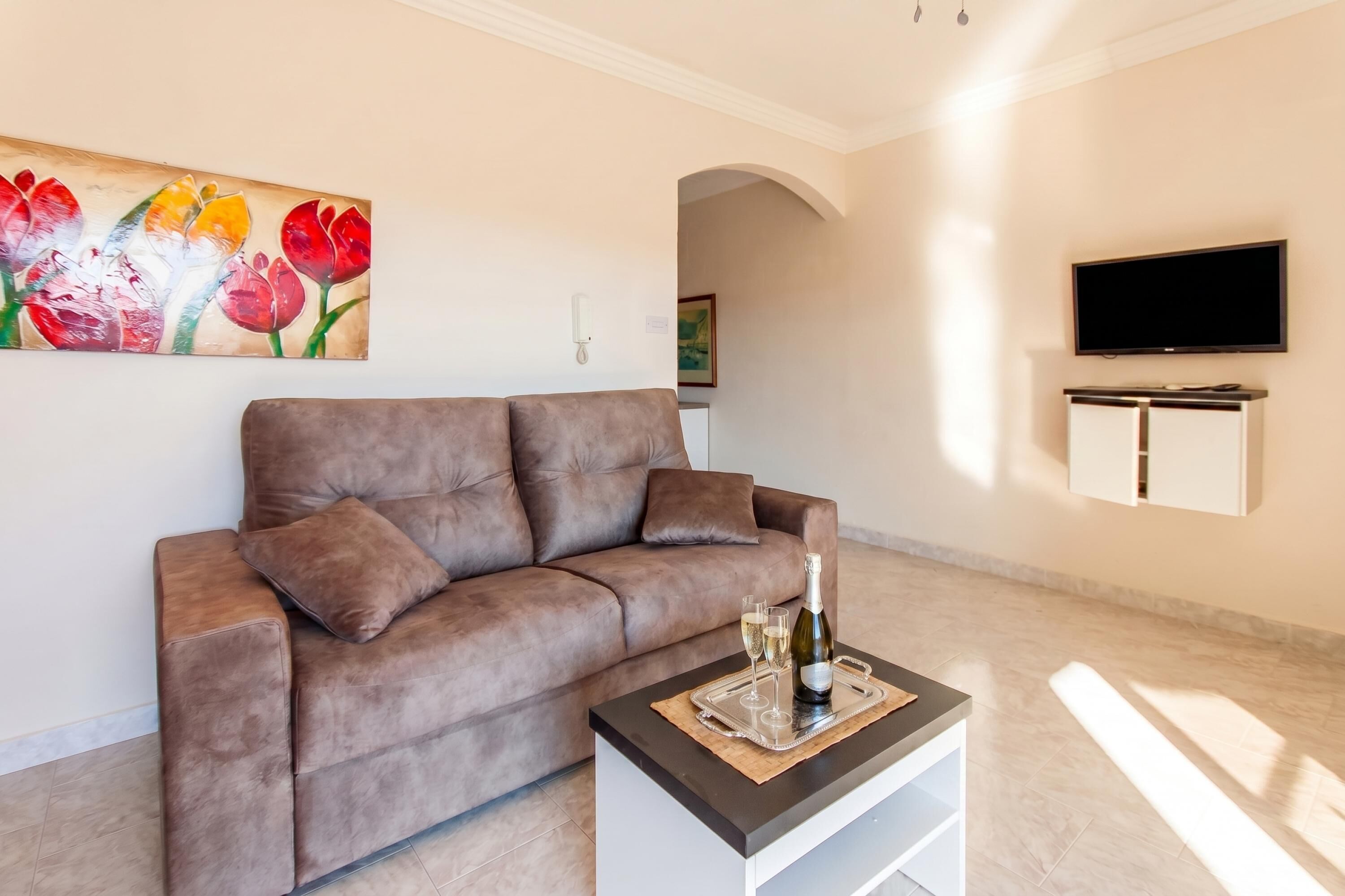 Ein Wohnzimmer mit einem braunen Sofa, einem Flachbildfernseher und einem Blumenbild.