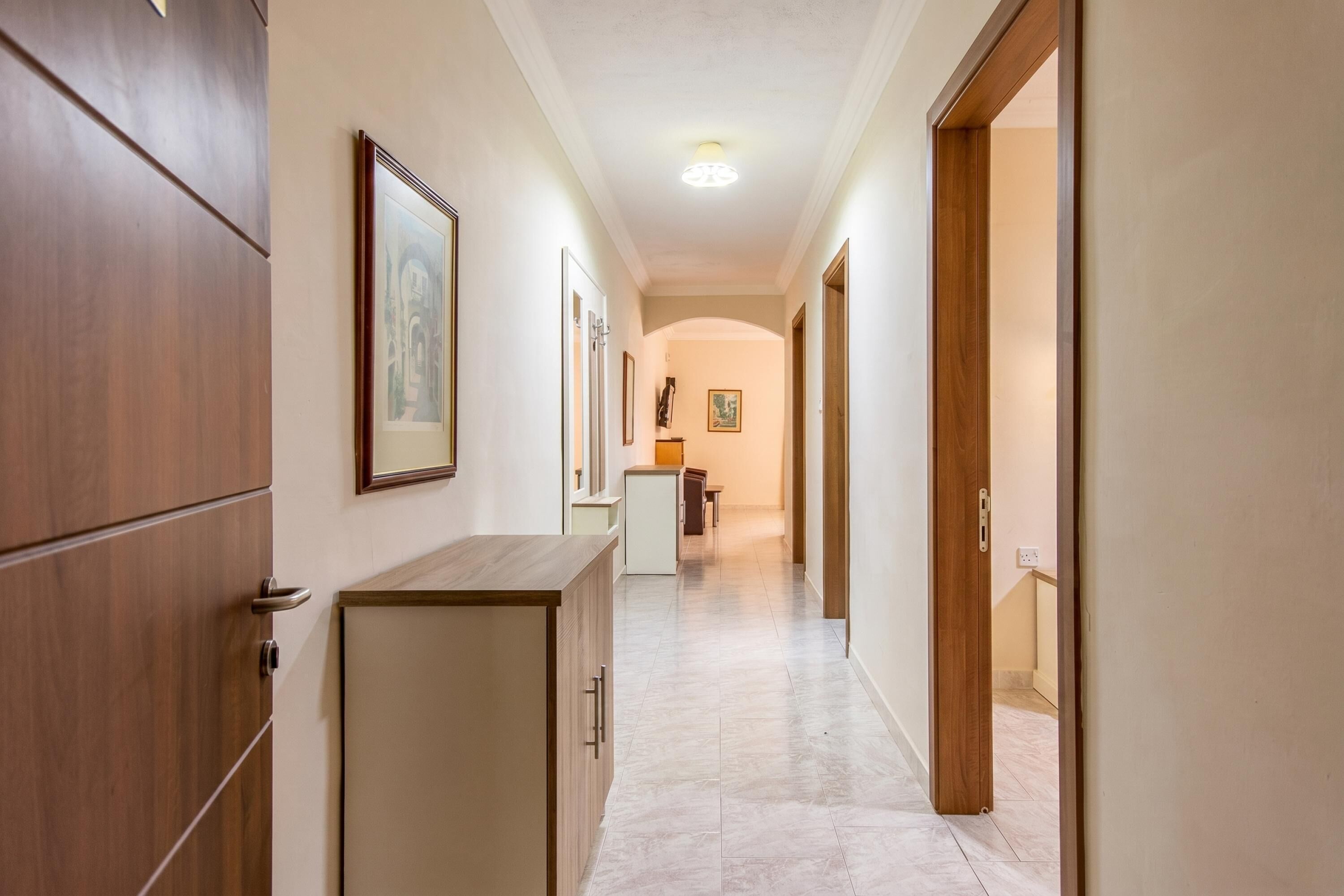 A hallway with wooden doors, framed artwork, a small table, and a staircase at the end.