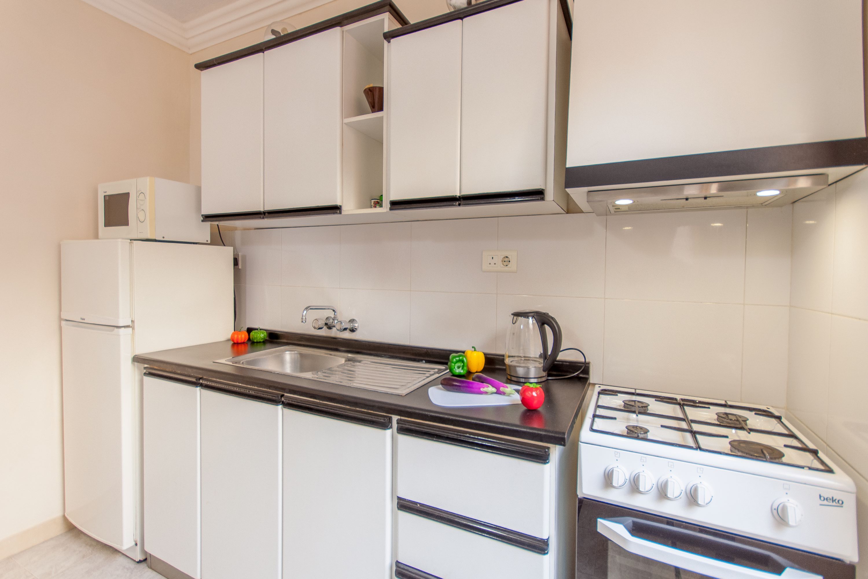 A kitchen with white cabinets, a stove, a sink, and a microwave.