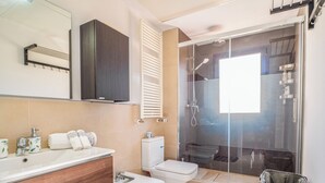 A modern bathroom with a wooden vanity, a white toilet, a glass-enclosed shower, and a towel rack.