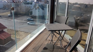 Een balkon met twee metalen stoelen en een tafel, met uitzicht op een straat met auto's en gebouwen.