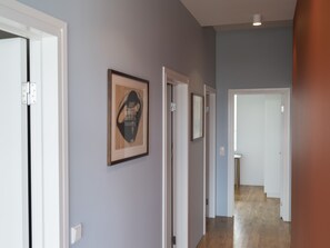 Un couloir avec des portes blanches, une œuvre d’art abstraite encadrée et un interrupteur sur le mur.