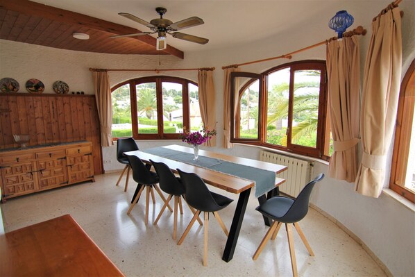 A dining area with a wooden table, black chairs, a ceiling fan, and large windows with curtains.